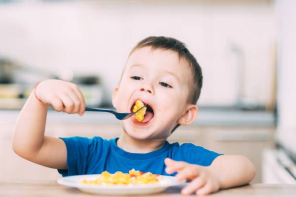 a child in a t-shirt in the kitchen eating an omelet, a fork